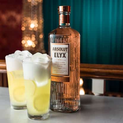 Copper Fizz in two highball glasses with lemon wheels and large ice beside an Absolut Elyx bottle on a bar