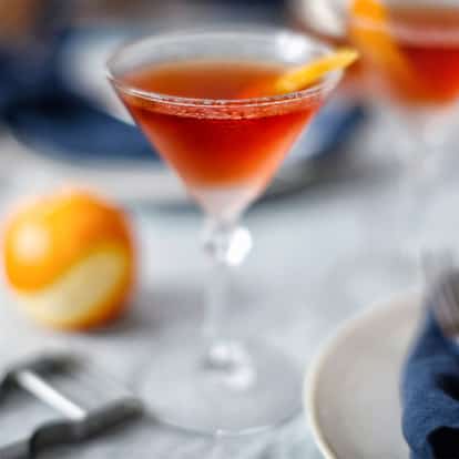 Corpse Reviver served in a martini glass with orange twist garnish on a table with peeled orange and napkin