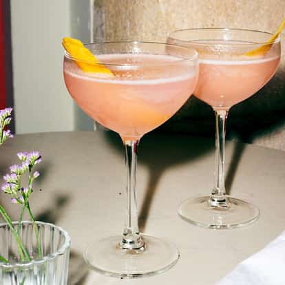 Cosmopolitan served in two coupe glasses with citrus peel garnishes.