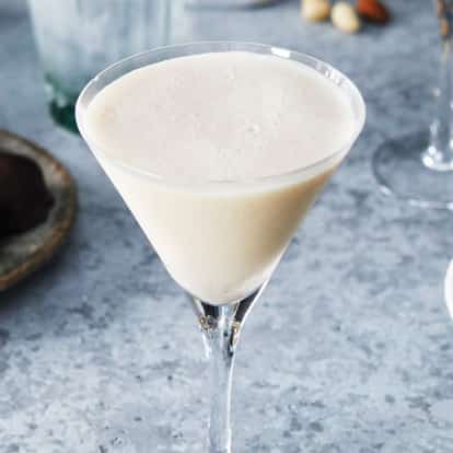 Cowboy served in a martini glass with foam on top beside chocolates and an espresso cup