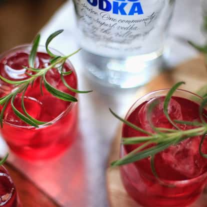 Cranberry Punch in three rocks glasses with ice and rosemary sprigs, vodka bottle in background