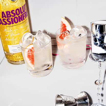 Crime of Passion in two rocks glasses with ice and grapefruit wedges beside an Absolut Passionfruit bottle on a sink