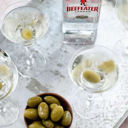 Classic Dirty Martini cocktail next to a bottle of Beefeater Gin and a bowl of green olives