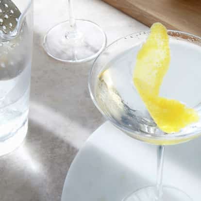 Classic Dry Martini garnished with a Lemon Twist next to a Julep Strainer.
