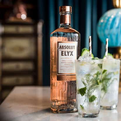Due Dilligence with an Absolut Elyx bottle and two iced highballs garnished with lime wedges and herb sprigs