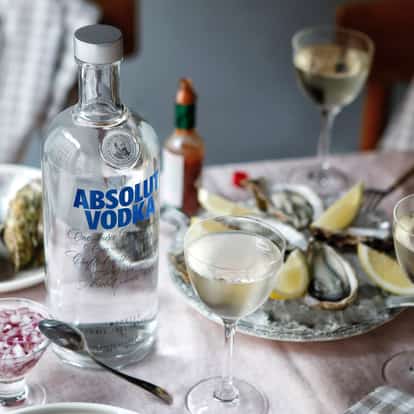 Elderflower Martini in coupe glasses with an Absolut Vodka bottle and a plate of oysters with lemon wedges on a table