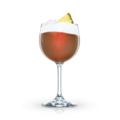 Elk’s Own Cocktail in a stemmed wine glass with crushed ice and a pineapple wedge on white background