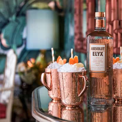 Elyx Redhead in three copper mugs with crushed ice and citrus garnish beside an Absolut Elyx bottle on mirrored bar