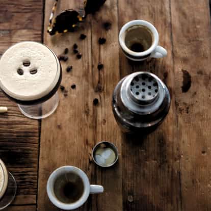 Espresso Button Fly in a coupe with three coffee beans on foam beside an Absolut bottle and espresso cups on wood