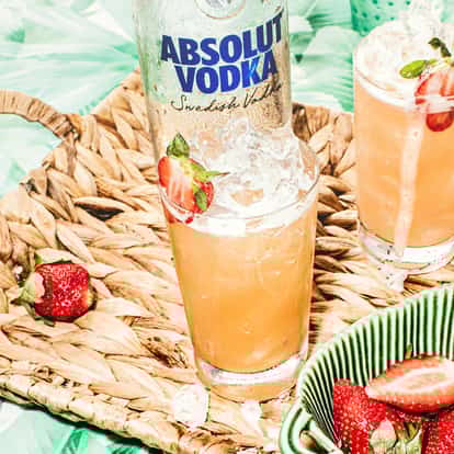 Exotic Passion tall glass with crushed ice and strawberry garnish and an Absolut Vodka bottle on a woven tray