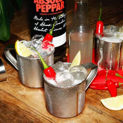 Fiery Mule three metal mugs with ice lemon wedges and chili peppers and an Absolut Peppar bottle behind