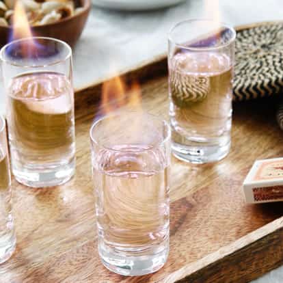 Flaming Sambuca in four shot glasses on a wooden tray with a matchbox