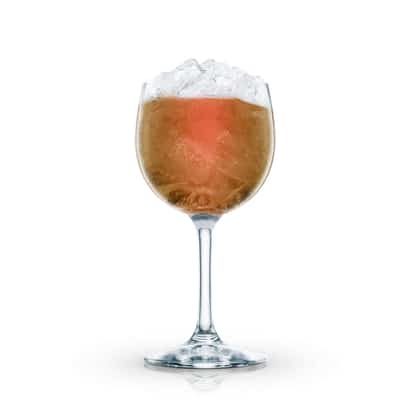 Single amber cocktail in a stemmed wine glass topped with crushed ice on white background.