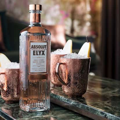 Fraise Prince Of Bel Air served in copper mugs with ice and pear slice alongside bottle of Absolut Elyx on marble table