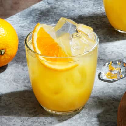 Gin And Orange in a lowball glass with ice and an orange slice on a stone surface