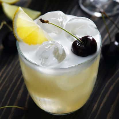 Gin Sour in a rocks glass with ice, a lemon wedge and a cherry