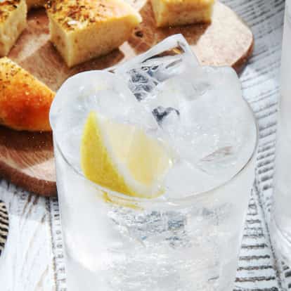 Gin Tonic in two highball glasses with ice and lemon wedges on a wooden table