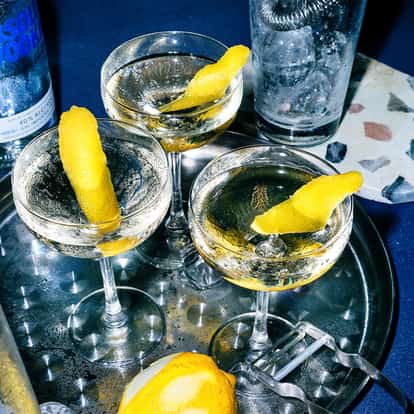 Good Dill Hunting cocktails sit in three coupe glasses with lemon twists beside an Absolut bottle on a tray.