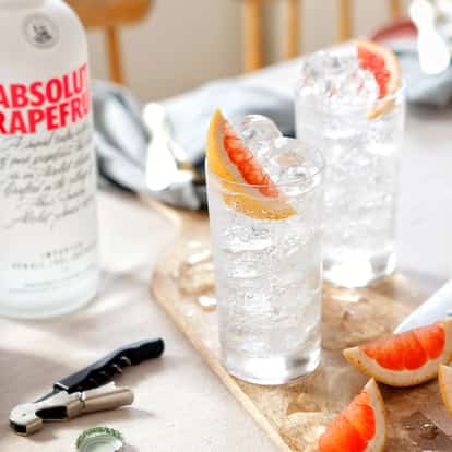 Grapefruit Vodka Soda in a highball glass with ice and a grapefruit wedge, Absolut Grapefruit bottle in background
