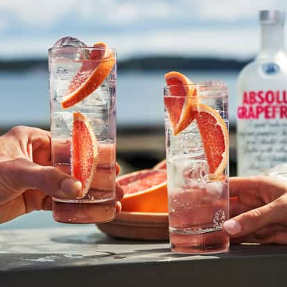 Grapefruit Vodka Tonic in highball glasses with ice, grapefruit wedges and an Absolut Grapefruit bottle behind