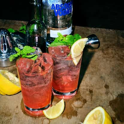 Grenadine Fizz in two highball glasses with ice, mint and lemon wedges and an Absolut vodka bottle on a table