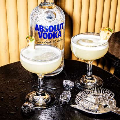 Two Hawaiian Cosmopolitan cocktails next to a bottle of Absolut Vodka.
