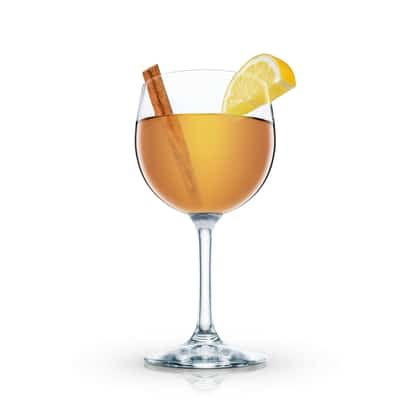 Hot Buttered Rum in a stemmed wine glass with cinnamon stick and lemon wedge on white background