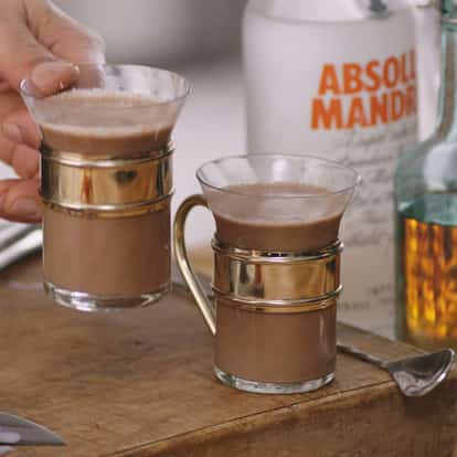 It's not Terry's in two glass mugs with metal holders on a wooden board with an Absolut Mandrin bottle in the background