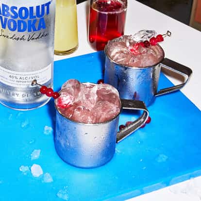 Jingle Mule in two hammered metal mule mugs filled with crushed ice and a cranberry skewer, Absolut Vodka bottle at left