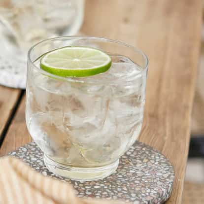 Lime Vodka Tonic on a wooden table in a rock glass garnished with a lime wheel.