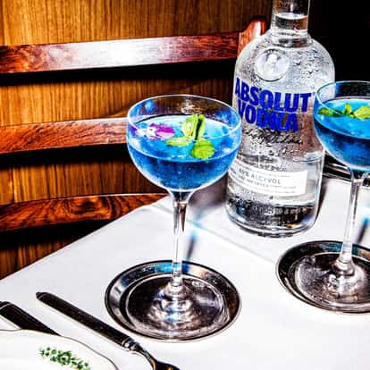 Lotus Flower Martini in coupe glasses with mint and edible flower garnish and an Absolut Vodka bottle on a tablecloth