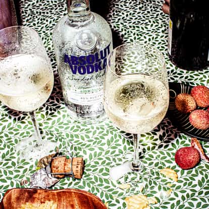Lychee Cooler served in two wine glasses with an Absolut Vodka bottle and lychees on patterned tablecloth
