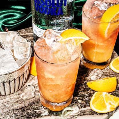 Madras in a highball glass with ice and an orange wedge and an Absolut vodka bottle behind on a round marble board