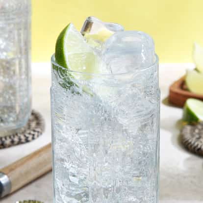 Malibu And Lemon-lime Soda in a highball glass with ice and a lime wedge on a tabletop