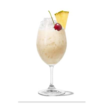 Malibu Piña Colada in a stemmed wine glass with crushed ice, pineapple wedge and cherry