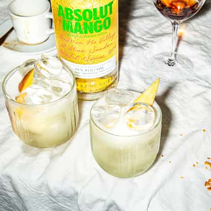 Mango Sour two rocks glasses topped with ice and orange peel and an Absolut Mango bottle behind
