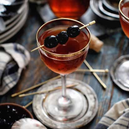 Classic Manhattan served in a cocktail glass, garnished with three Maraschino Cherries.