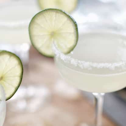 Classic Margarita cocktail in a Margarita glass with a salt rim and garnished with a lime wheel.