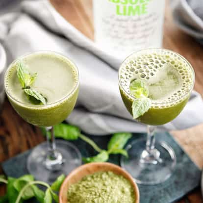Matcha Cocktail served in two coupe glasses garnished with mint with an Absolut Lime bottle in the background
