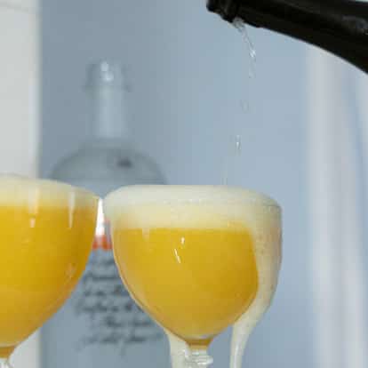 Matilda in two coupe glasses with foamy heads as a bottle pours into the right glass