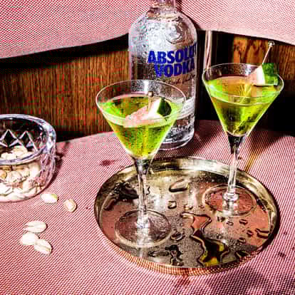 Melon Martini in martini glasses with melon wedges on a metal tray and an Absolut Vodka bottle behind