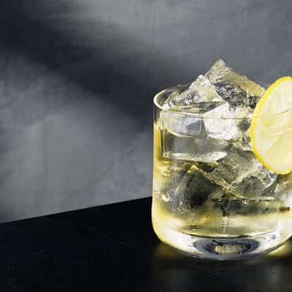 Midsommer Holiday in a rocks glass with ice and a lemon wheel on black background