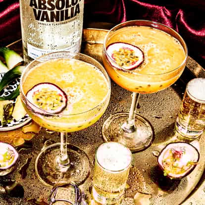 Passion Star Martini served in two coupe glasses garnished with halved passion fruit on tray with Absolut Vanilia bottle