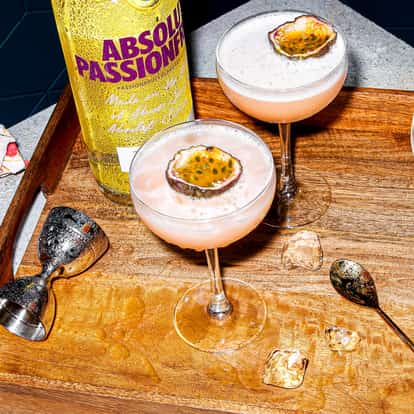 Three martinis in coupe glasses garnished with halved passionfruit and an Absolut Passion bottle.