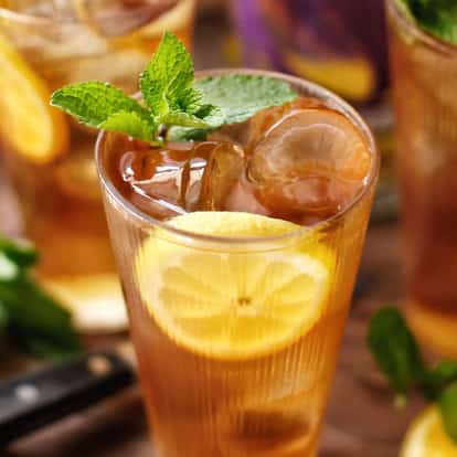 Passionfruit & Peach Iced Tea served in a tall glass with ice lemon slices and a mint sprig