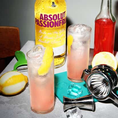 Passionfruit Collins served in three Collins glasses with lemon peels and ice and an Absolut Passionfruit bottle