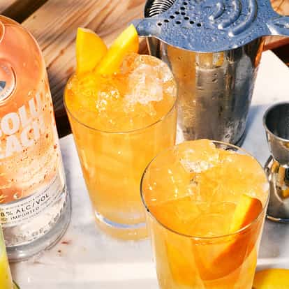 Peach On The Beach served in two highball glasses with peach slices beside an Absolut Peach bottle.