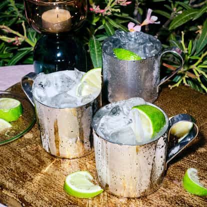 Pear and Elderflower Mule served in three metal mule mugs with ice and lime wedges on a wooden board