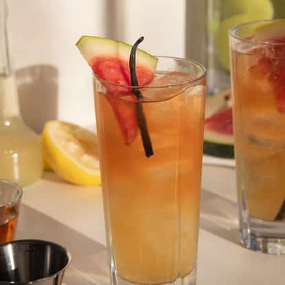 Peary Afternoon in a tall highball glass with ice and a watermelon wedge and vanilla bean garnish
