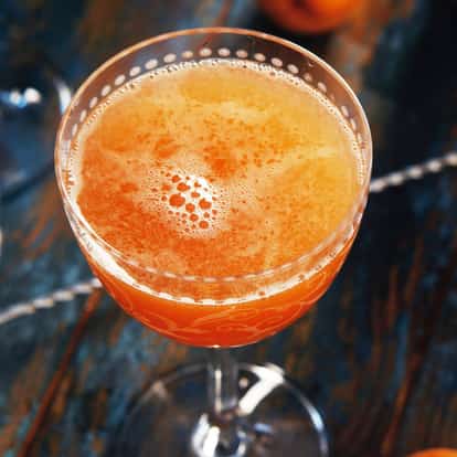 Pendennis Cocktail in a stemmed coupe glass with froth on top and a bitters bottle nearby